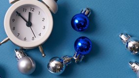 Blue and silver christmas balls, white alarm clock on a blue paper background. Ten minutes before new years. Minimal christmas celebration concept