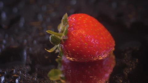 The slow-motion fall of one strawberry on a wet, black mirror surface. Macro shooting of berries.