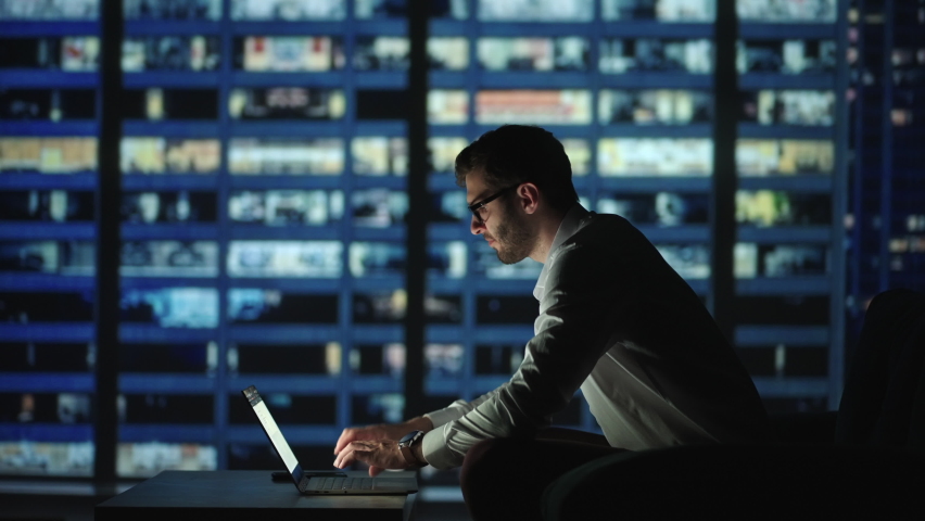 Tired young man working on a laptop late night in the office. Sleepy Businessman sitting at desk in dark office. Tired and stressed businessman in glasses works on a laptop of the night city office Royalty-Free Stock Footage #1078998263