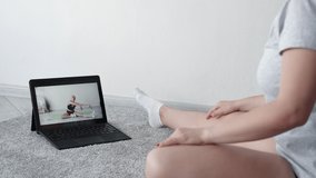 Home training. Fitness blog. Healthy body. Sport program. Unrecognizable woman doing stretching workout watching laptop with fit lady in light room interior.