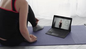 Fitness blog. Sportive woman. Online training. Video lesson. Unrecognizable lady sitting floor watching dance workout for hands with female trainer on laptop in light room interior.