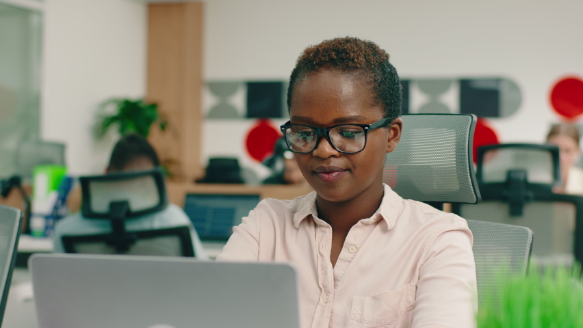 A very clever and charming young black woman with glasses is at her large office, sitting at the table and smiling greatly Royalty-Free Stock Footage #1079008919