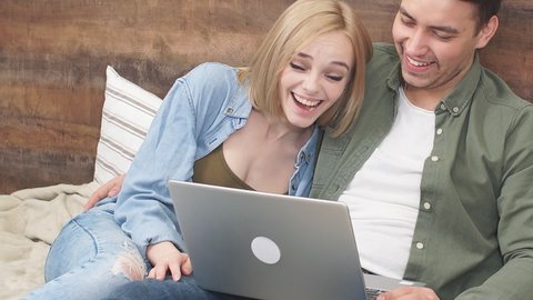 Happy Young couple watches movie on laptop lying on bed in their bedroom.