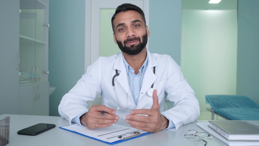 Indian latin male happy positive gp doctor in modern clinic wearing white coat uniform talking using laptop computer having videocall chat, consulting remotely. Telemedicine concept. Webcam view.