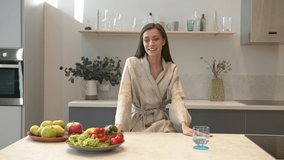Food blogger, attractive woman standing on background of kitchen room, table with plates of fresh fruits and vegetables. Vegan lifestyle and diet, gimbal shot
