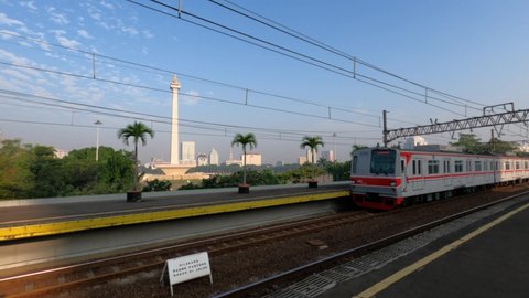 Jakarta, Indonesia - August 14, 2021: The KRL Commuter Line train passes through the Gambir Railway Station with the Monas National Monument as a background in the morning. Flat color profile.