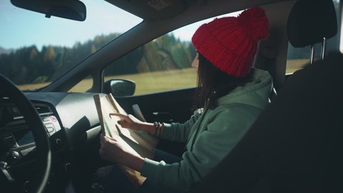 Pretty girl studying the map and sitting in car during her roadtrip after long quarantine self isolation. Woman during social distancing and solo activity concept. Active and positive lifestyle.