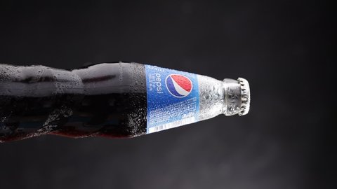 DNIPRO, UKRAINE - JULY 19, 2021: Glass bottle of Pepsi rotates on a dark background. Popular american drink revolves around its axis. Vertical format