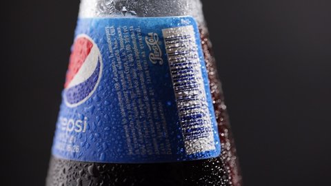 DNIPRO, UKRAINE - JULY 19, 2021: Glass bottle of Pepsi rotates on a dark background. Popular american drink