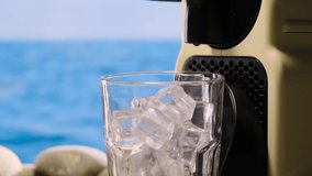 Close up iced coffee early morning at sea, making latte on vacation by ocean. Beige capsule coffee machine makes coffee in transparent mug or cup with ice. relaxing on beach, in background blue water. - Powered by Shutterstock - Get 15% off with code: PIKWIZARD15