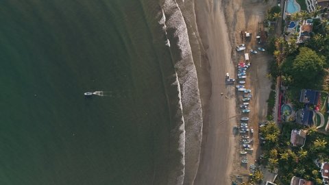 Descending top down aerial as lone fishing boat leaves beach in morning, 4K
