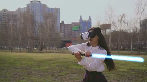 Modern VR technology play. Female virtual reality warrior fencing with lightsaber laser sword. Augmented reality goggles. Fence practicing woman in Scott pattern skirt in futuristic headset gadget.