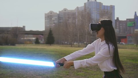Modern VR technology play. Female virtual reality warrior fencing with lightsaber laser sword. Augmented reality goggles. Fence practicing woman in Scott pattern skirt in futuristic headset gadget.