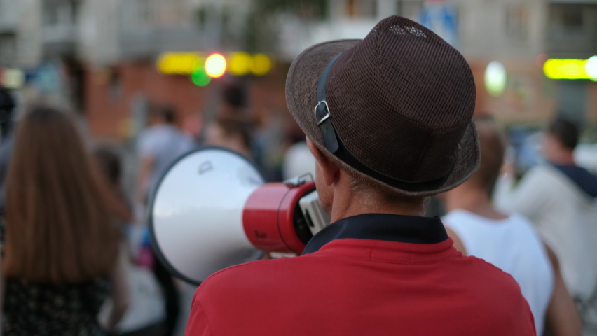 Strike activist demonstrator man on opposition rally riot with megaphone walks. Political protester guy with bullhorn marches in protest crowd. Male rebel speaking on demonstration revolt resistance. Royalty-Free Stock Footage #1079041211