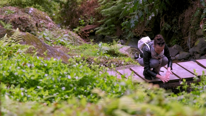 A tourist passing a wooden bridge is wetting hands in a forest creek, Sao Miguel island, Azores, Portugal