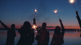 Cheerful friends men and women are dancing and waving sparklers enjoying warm summer nights outdoors on beach. Youth and leisure activities concept. - Powered by Shutterstock - Get 15% off with code: PIKWIZARD15