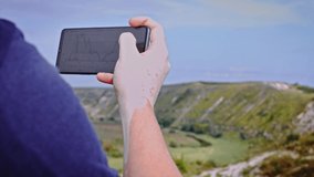 The man is watching the Bitcoin exchange on the phone. It is in a place on the rocks. Symbol of faith. 4k video