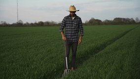 Mixed race male farmer walking through wheat fields with pitch fork