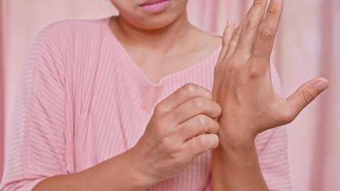 Annoyed middle-aged woman scratching itch on her hand from itchy dry skin, eczema, dermatitis, allergy, psoriasis. Health care and skin disease concept.