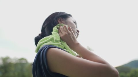 Young asian woman using towel on neck wiping sweat on face and neck during exercise at green park, take a break from training, woman drying sweat, tiredness and sport concept, active healthy lifestyle