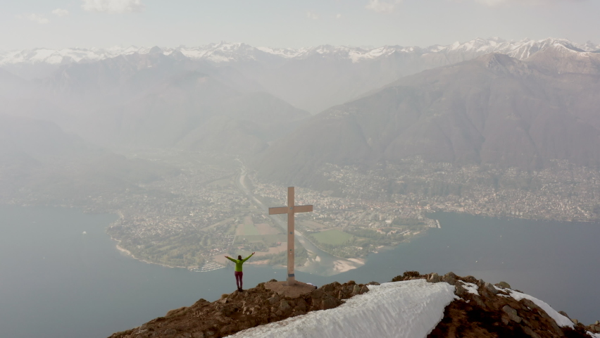 Drone aerial shot of young woman hiking reaching the mountain top. Spectacular views of lake and mountain, female on a hike. Shot with a drone 