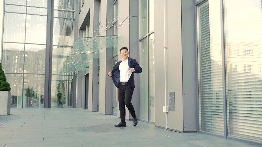 Cheerful happy asian business man dancing walk the corridor backdrop a modern office building, outside, outdoors Funny successful businessman in suit rejoices joyfully jump celebrates victory, success Royalty-Free Stock Footage #1079071583