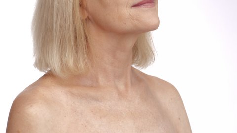 Anti aging body care. Close up shot of unrecognizable senior woman stroking her neck and neckline, enjoying smooth skin, posing with bare shoulders, white studio background