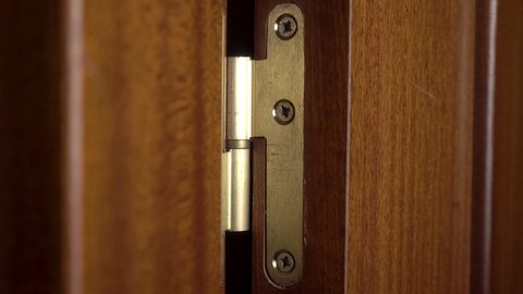 Using a golden door hinge. Screw caps with grime. Wooden brown dark door. Close-up.