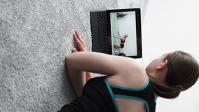 Fitness blog. Online lesson. Home training. Strong body. Unrecognizable woman watching laptop with female trainer showing correct plank workout in light room interior vertical.