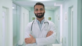Smiling happy cheerful male Indian latin doctor medical worker in white robe with stethoscope around neck standing in modern hospital clinic with arms crossed looking at camera. Headshot portrait. - Powered by Shutterstock - Get 15% off with code: PIKWIZARD15