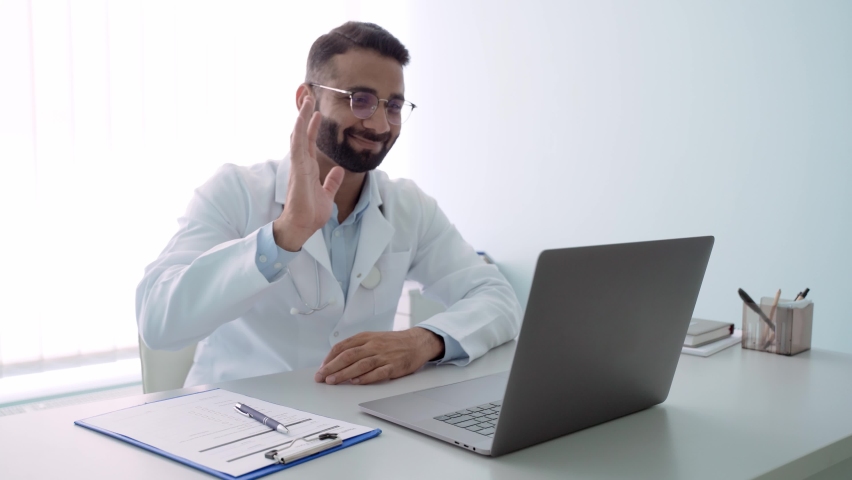 Indian male happy cheerful doctor therapist in modern clinic wearing eyeglasses and white coat uniform talking using laptop computer having videocall chat, consulting remotely. Telemedicine concept. Royalty-Free Stock Footage #1079079947