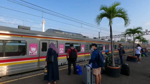 Jakarta, Indonesia - August 14, 2021: Passengers waiting train on the platform at Gambir Railway Station as the KRL electric train passes. With a Monas National Monument as background in the morning.