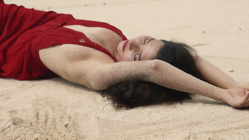 Beauty, travel, fashion concept and lifestyle. fashion beautiful sensual woman with dark hair in elegant red dress lying on beach. Asian stunning sexy female lying and relaxing on white sand.
