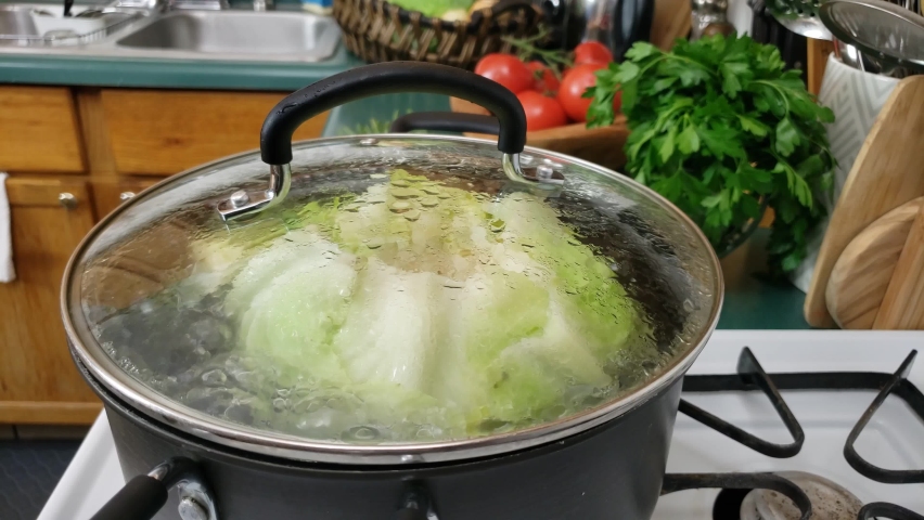 Home cooking - Close up of whole cabbage being boiled or blanched in pot of water for ease leaf removal. Royalty-Free Stock Footage #1079081576