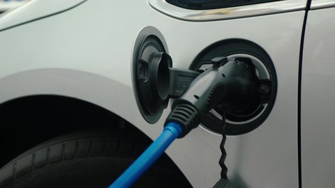 Male hand disconnects power connector into EV car. Unrecognizable man unplugs charging cable electric vehicle