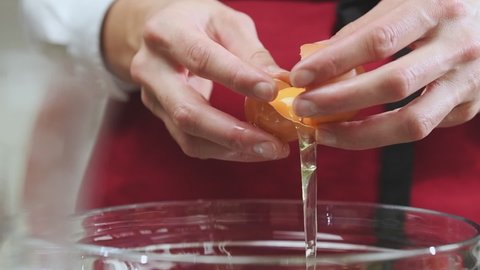 Female hands separate the egg white from the yolk over a glass bowl.