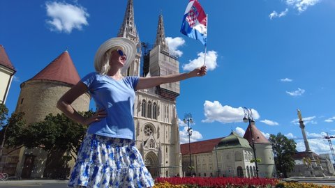 Smiling girl with Croatian flag in the square of Zagreb Cathedral of Zagreb city, capital of Croatia in Europe. Colonnade monument of the Assumption of the Blessed Virgin Mary.