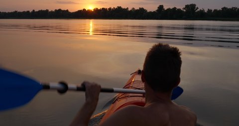 A man kayaks on a calm river towards the sunset. He skillfully rowing oar. Beautiful nature of the evening river. Slow Motion Ultra 4K 