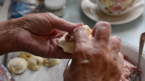 An elderly woman makes dumplings from dough and minced meat at home. Home cooking, DIY cooking, natural and healthy food.
