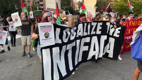 NYC, USA - SEPT 12, 2021: protestors marching with Globalize the Intifada sign at Palestinian rights protest - Empire State Building in background - activists in New York City.