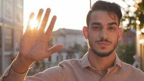 Male portrait outdoors in city young adult serious attractive bearded business man arab boss leader guy in shirt stands on street looking at camera holds hand on background of sunset sunbeams sun rays