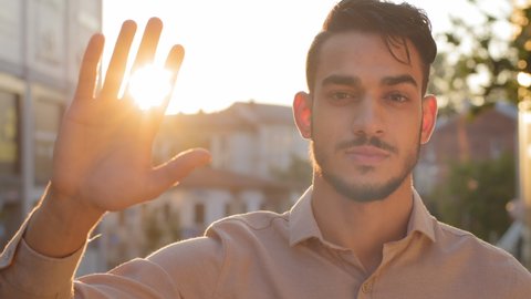 Male portrait outdoors in city young adult serious attractive bearded business man arab boss leader guy in shirt stands on street looking at camera holds hand on background of sunset sunbeams sun rays