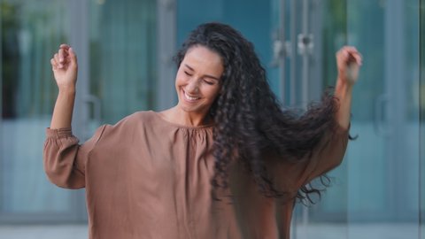 Beautiful happy cheerful young hispanic woman brunette with curly hairstyle caucasian attractive girl model dancing in city on street moving head with long hair enjoy weekend rejoicing dance active