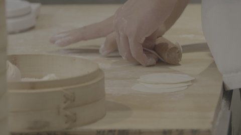 A person kneading chinese dumplings dough with a rolling pin. close up, hands