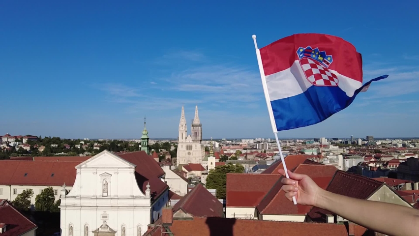 SLOW MOTION: Woman hand with Croatian flag by top view of Zagreb city, capital of Croatia, from panoramic terrace of bell tower. Aerial view of cityscape with Zagreb Cathedral in the distance.