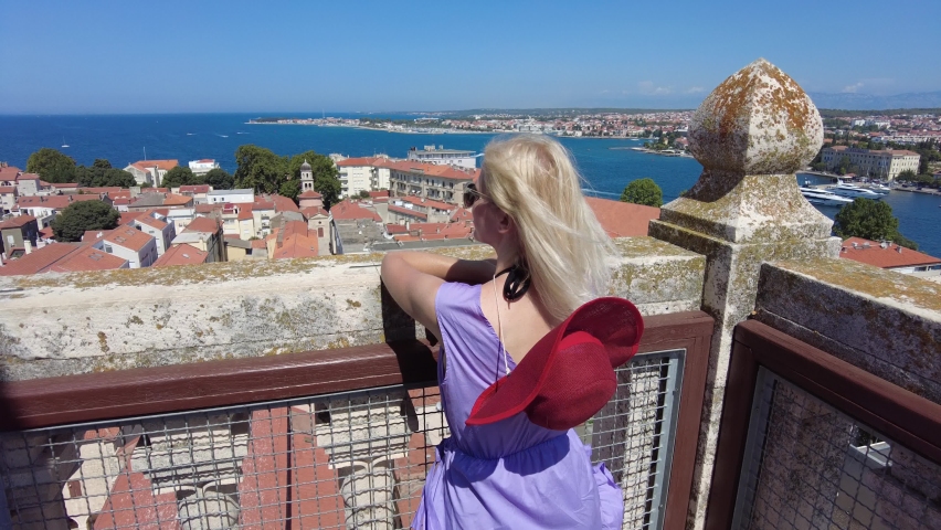 Woman with hat on top view of Zadar city of Croatia on Adriatic Sea and capital of Dalmatia. Panoramic terrace of Cathedral bell tower. Aerial view of the cityscape in summer.
