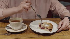 The girl takes a piece of cake with a fork, then drinks black tea from a cup, sitting in a cafe. Close up shot.