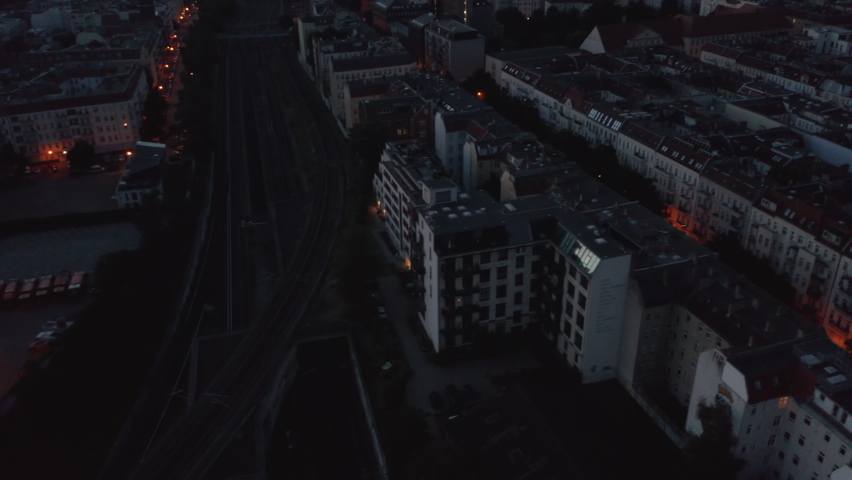 Fly above blocks of residential buildings. Tilt up reveal view of city before sunrise. Colourful twilight sky. Berlin, Germany