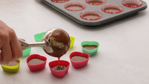 Scooping chocolate batter into a silicon molds, close up video, chocolate cupcakes recipe