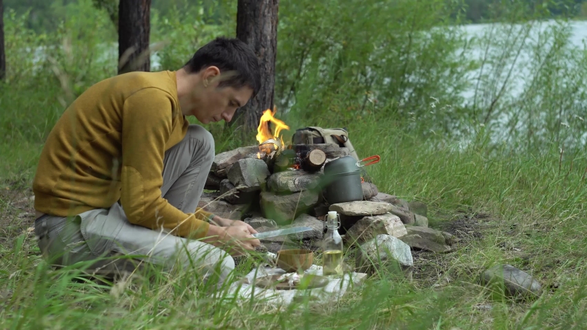 Man in the forest by the fire is cutting vegetables for cooking. Concept of survival skills in the wild, hiking
